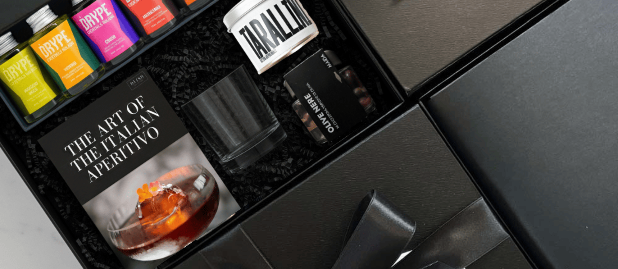 DLISH curated Italian corporate gift box featuring The Art of the Italian Aperitivo book, BRYPE bitters, Tarallini, and Olive Nere on dark background