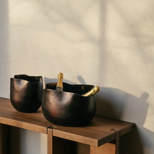 Two Gravity champagne coolers in bronze aluminium on an oak console, one holding bottles of champagne
